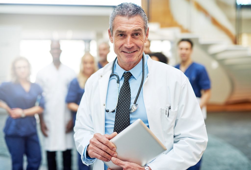 Cheerful mature doctor with tablet in hospital